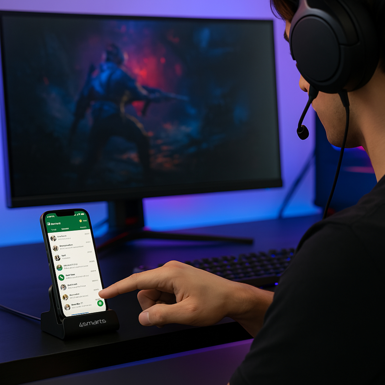 Person with gaming headset uses smartphone on 4smarts charging station in front of monitor with video game – the perfect setup for any gaming desk.